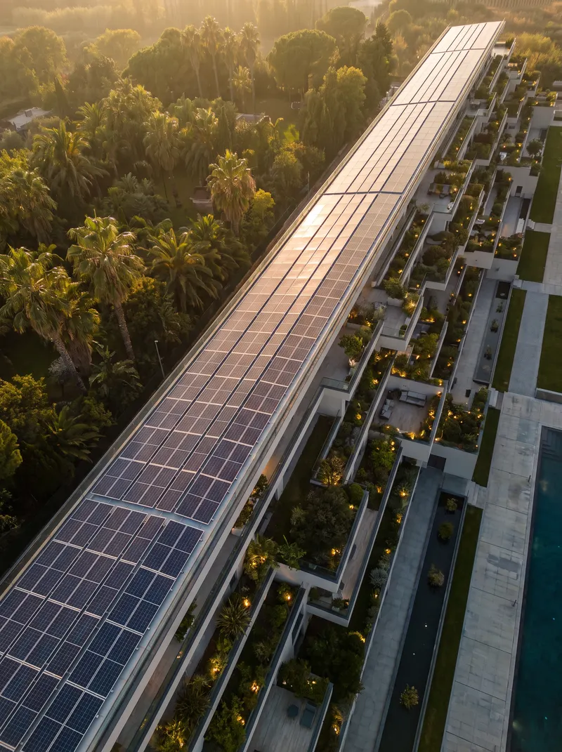 Aerial view of a terraced building with a solar panel roof and planted terraces among palms